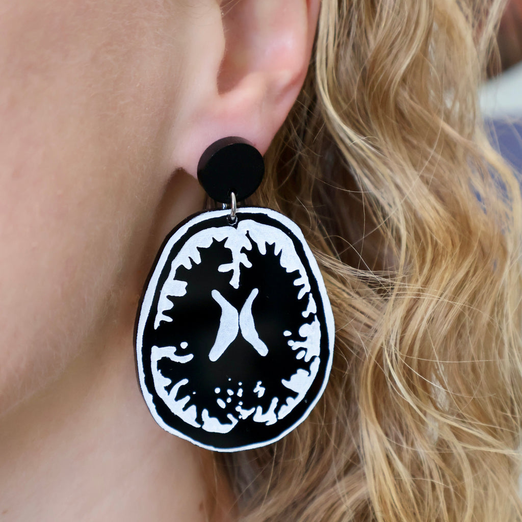 Black and white statement sized MRI brain earrings being modelled. Laser cut from acrylic.