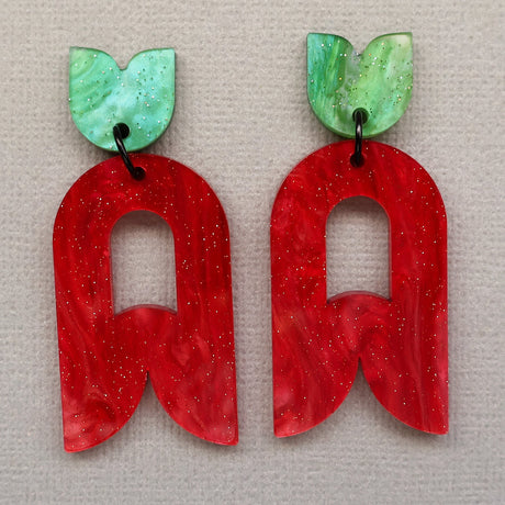 Closeup view of Red and green abstract flower earrings on a greybackground