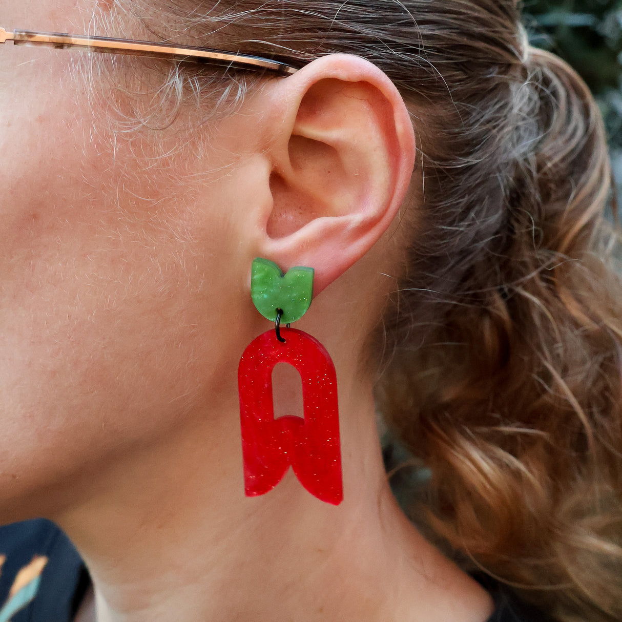 Close-up of a person wearing abstract flower earrings in red and green.
