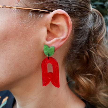 Close-up of a person wearing abstract flower earrings in red and green.