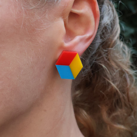 Colourful red, blue and yellow geometric cube stud earring worn by a person