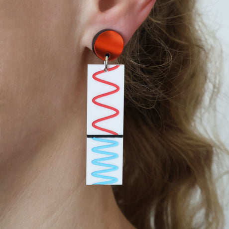 Rectangular earring with red and blue wavy line design depicting the doppler effect worn by a person