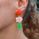 Close-up of a person wearing colourful floral acrylic earrings earrings. The earrings contain 2 flowers and a leaf. 