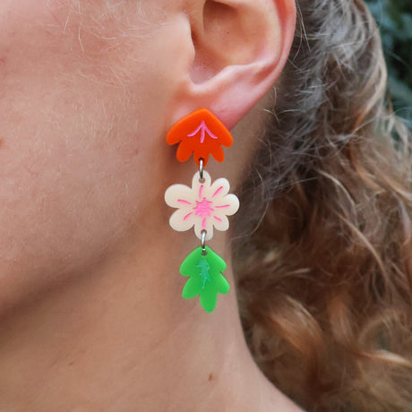 Close-up of a person wearing colourful floral acrylic earrings earrings. The earrings contain 2 flowers and a leaf. 