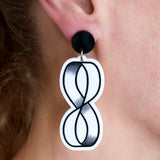Black and white acrylic dangle earrings with mobius strip design being modelled on ear. 