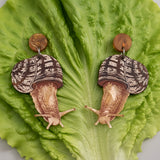 Acrylic snail earrings sitting on a green lettuce leaf. 