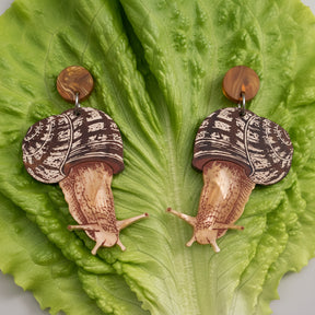 Acrylic snail earrings sitting on a green lettuce leaf. 