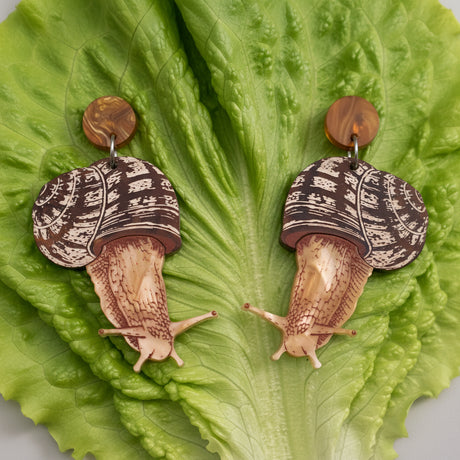 Acrylic snail earrings sitting on a green lettuce leaf. 