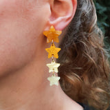 Closeup of a person wearing acrylic star earrings. 4 stars in 4 different yellow and gold toned acrylics are stacked. 