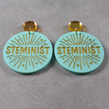 Turquoise or teal dangle earrings with 'STEMINIST' gold text and gold mirror acrylic toppers