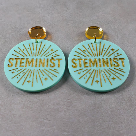 Turquoise or teal dangle earrings with 'STEMINIST' gold text and gold mirror acrylic toppers