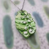 Angled view of green acrylic tardigrade pendant showing 3 dimensional construction.