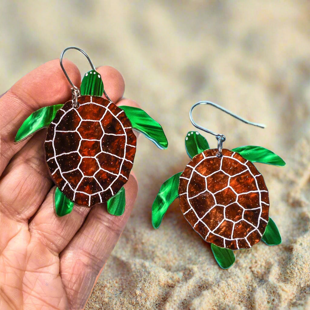 Acrylic turtle earrings held by a hand on a light blue background