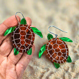 Acrylic turtle earrings held by a hand on a light blue background
