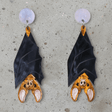 A pair of acrylic vampire bat earrings, hanging upside down from light pink/blue round acrylic toppers. 