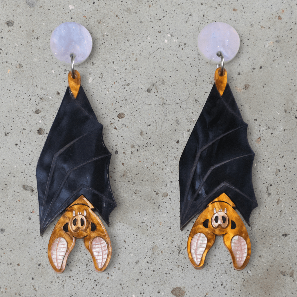A pair of acrylic vampire bat earrings, hanging upside down from light pink/blue round acrylic toppers. 