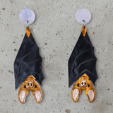A pair of acrylic vampire bat earrings, hanging upside down from light pink/blue round acrylic toppers. 