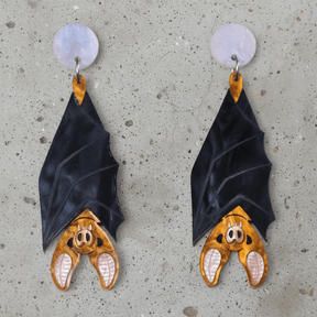 A pair of acrylic vampire bat earrings, hanging upside down from light pink/blue round acrylic toppers. 