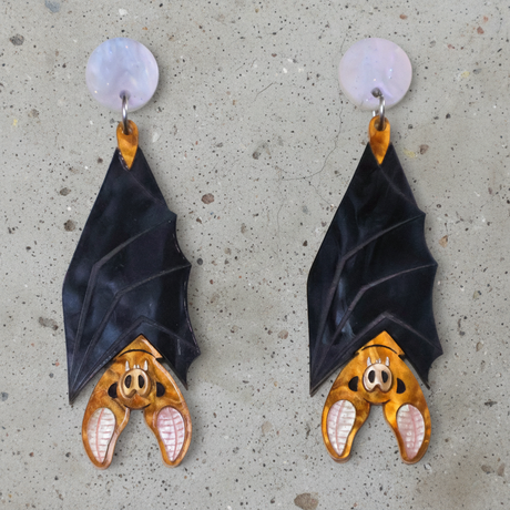 A pair of acrylic vampire bat earrings, hanging upside down from light pink/blue round acrylic toppers. 