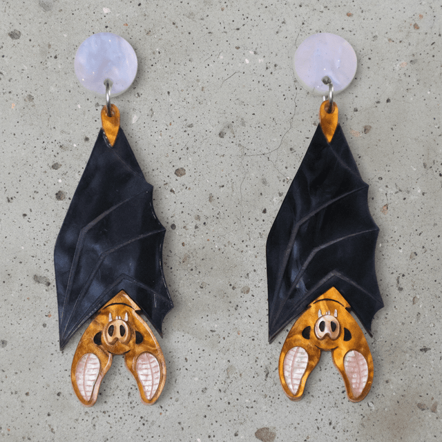A pair of acrylic vampire bat earrings, hanging upside down from light pink/blue round acrylic toppers. 