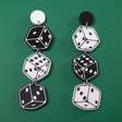 A pair of black and white earrings with a dice design. 3 dice hang from round earring toppers. 