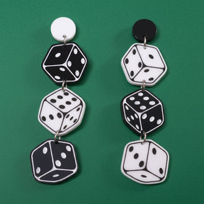 A pair of black and white earrings with a dice design. 3 dice hang from round earring toppers. 