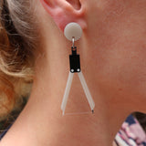 Close-up of an earring shaped like a drawing compass being worn by a person.