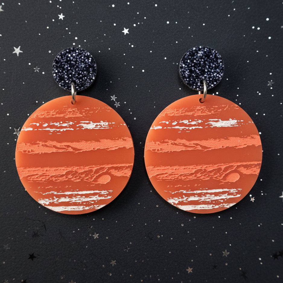 A pair of earrings with an orange jupiter design, hanging from back glitter toppers. 