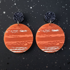 A pair of earrings with an orange jupiter design, hanging from back glitter toppers. 