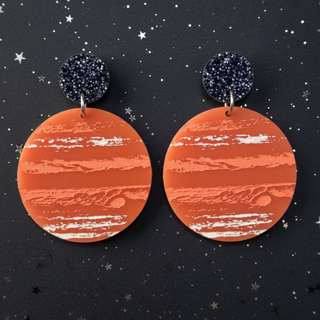 A pair of earrings with an orange jupiter design, hanging from back glitter toppers. 