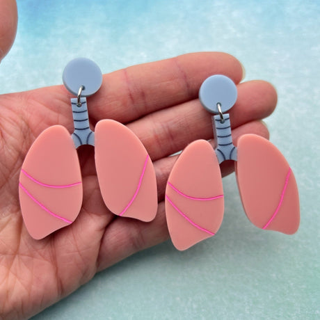 Pair of pink lung-shaped earrings  held in a hand against a light blue background.