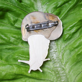 A closeup image of the back side of an acrylic snail brooch, showing the stainless steel brooch pin with rolling clasp. 