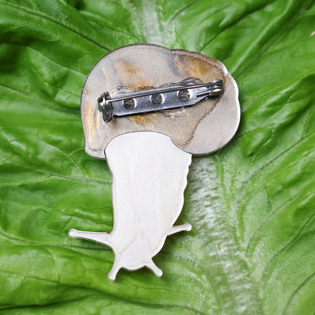 A closeup image of the back side of an acrylic snail brooch, showing the stainless steel brooch pin with rolling clasp. 