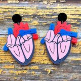 A pair of anatomical heart earrings, showing a cross-sectional view. Made from laser cut and handpainted acrylic.