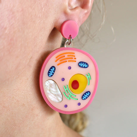 A laser cut acrylic animal cell themed dangle earring being modelled, showing it's intricate detail. The other half f the pair, an asymmetrical plant cell earring, in not shown. 