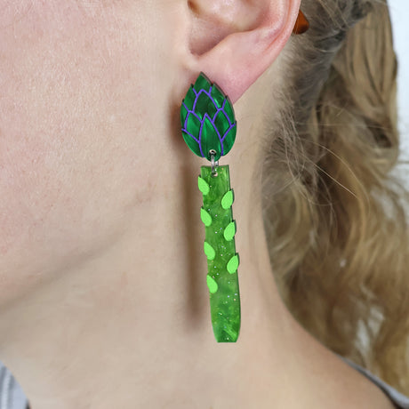 Green asparagus acrylics earrings worn by a person with blonde hair.