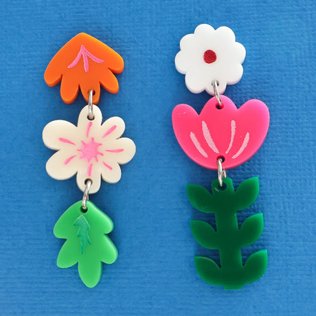 Pair of colourful asymmetrical acrylic floral earrings on a blue background