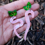 Pink asymmetrical worm-shaped earrings with green leaf tops held in a hand against a natural background.