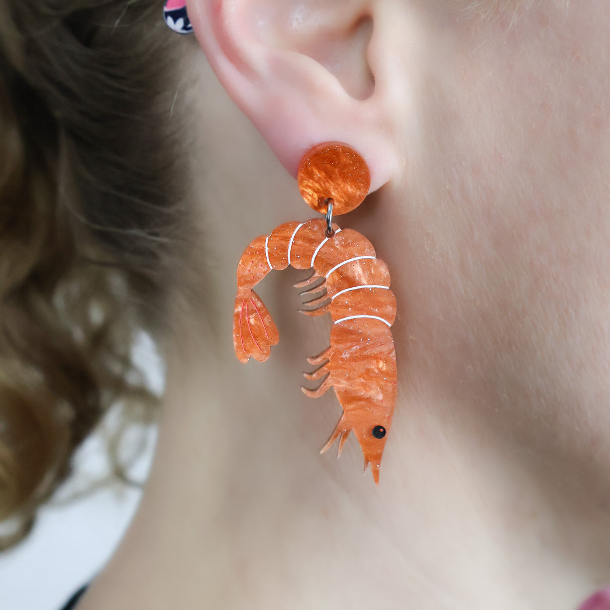 Laser cut acrylic orange shrimp earrings, being modelled. 