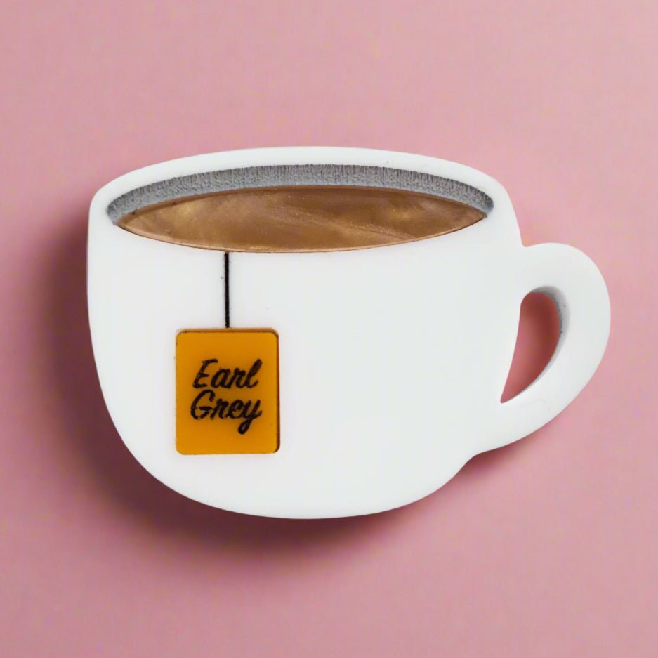 Closeup view of Earl Grey Tea Acrylic Brooch Pin, depicting a teabag hanging from a white cup.