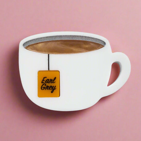 Closeup view of Earl Grey Tea Acrylic Brooch Pin, depicting a teabag hanging from a white cup.