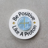 Circular brooch with 'Be Positive Like A Proton' text and a blue 'proton' in the centre