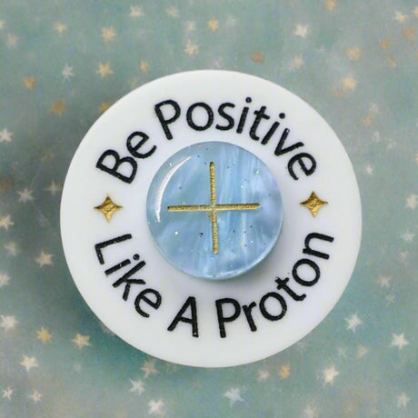 Circular brooch with 'Be Positive Like A Proton' text and a blue 'proton' in the centre