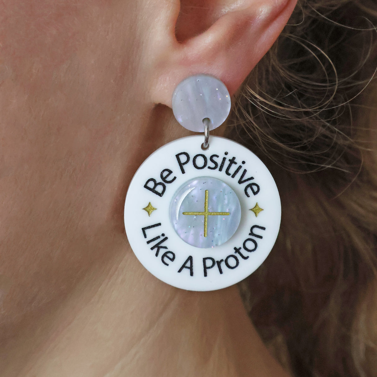 Earring with 'Be Positive Like A Proton' text worn by a person