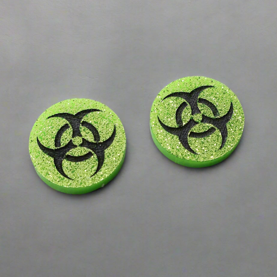 Small green glitter acrylic biohazard studs with black hand painted detailing. 