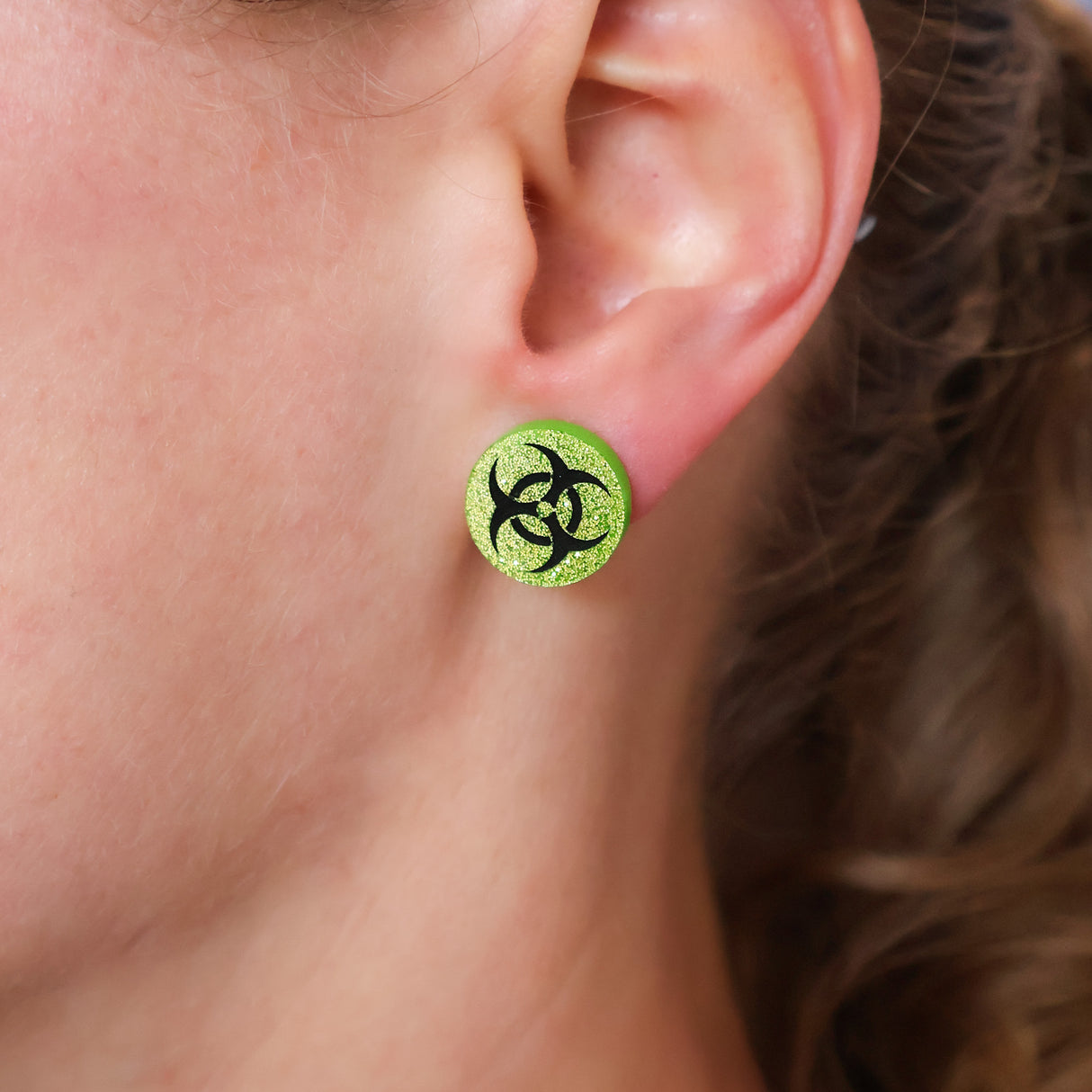 Close-up of an ear wearing a green stud earring with a biohazard symbol.
