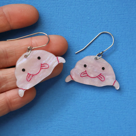 A pair of pink acrylic blobfish earrings being held in a hand.