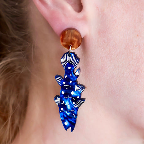 Blue acrylic coelocanth dangle earrings with brown toppers being worn