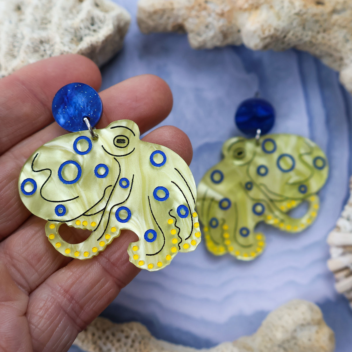 Laser cut acrylic blue ringed octopus earrings, being held up.