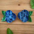 A pair of marbled acrylic blueberry studs with green leaves on a grey background
